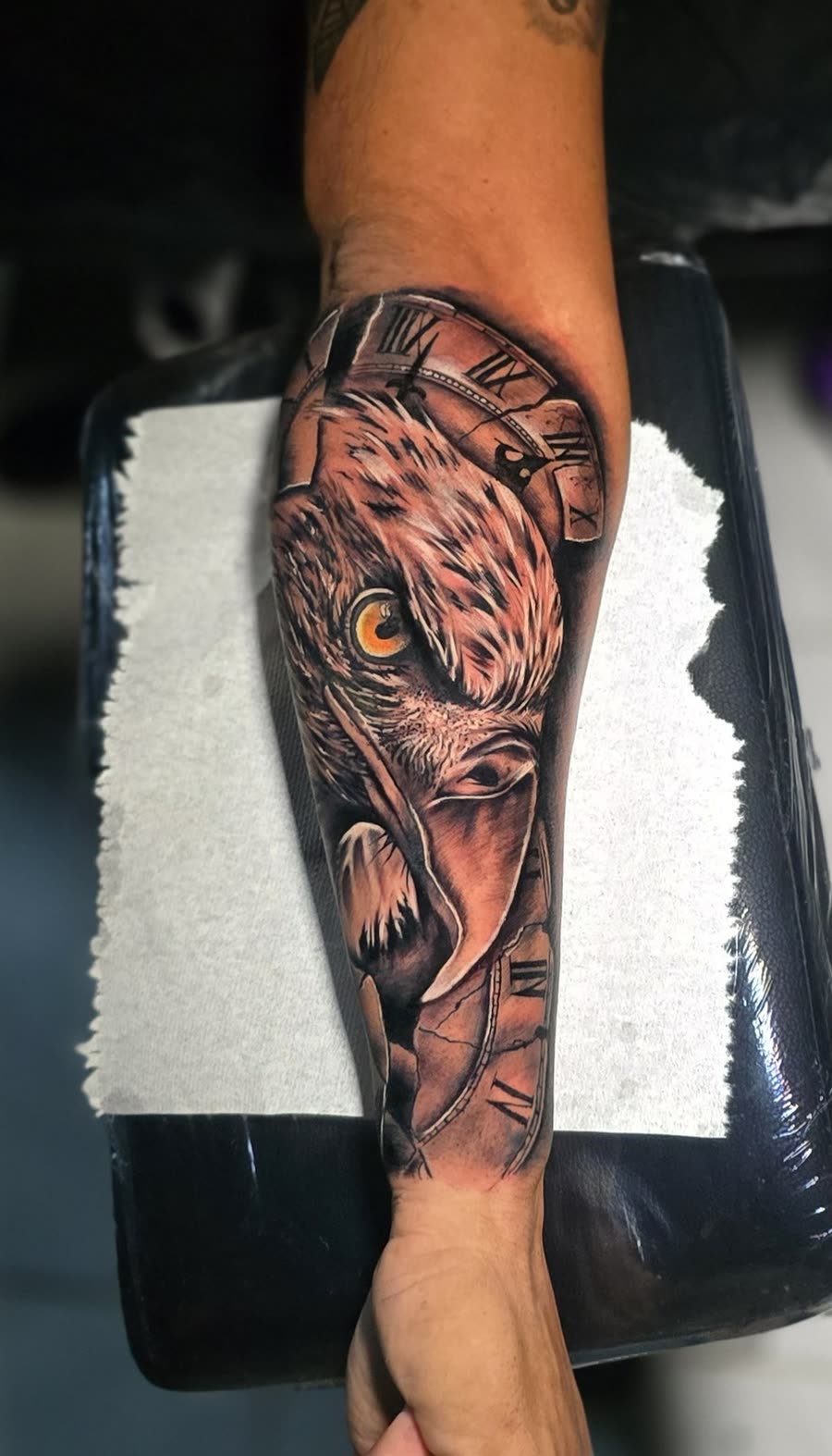 Águila con reloj roto y ojo naranja en antebrazo