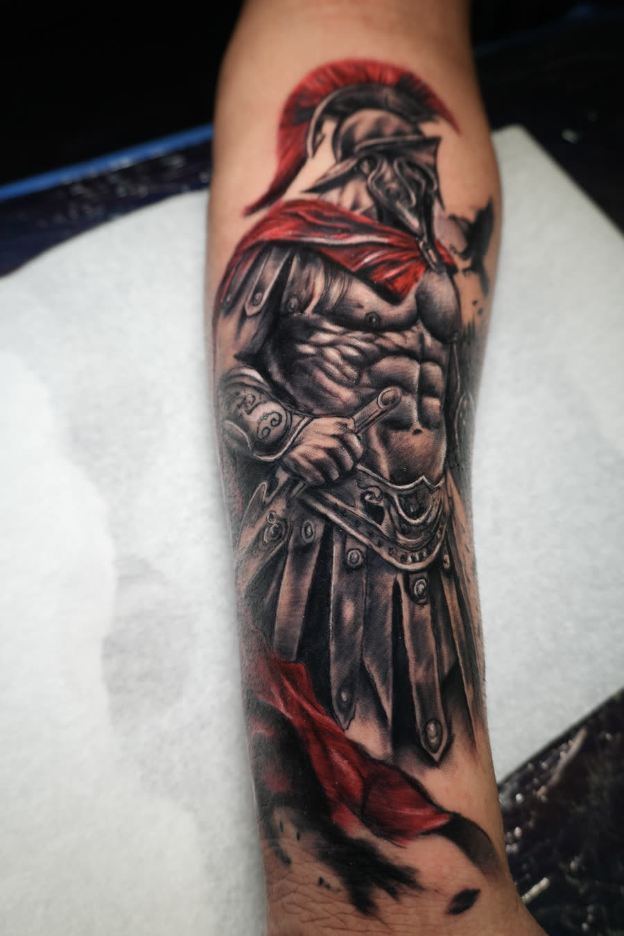 Guerrero espartano con capa y cresta rojas en antebrazo